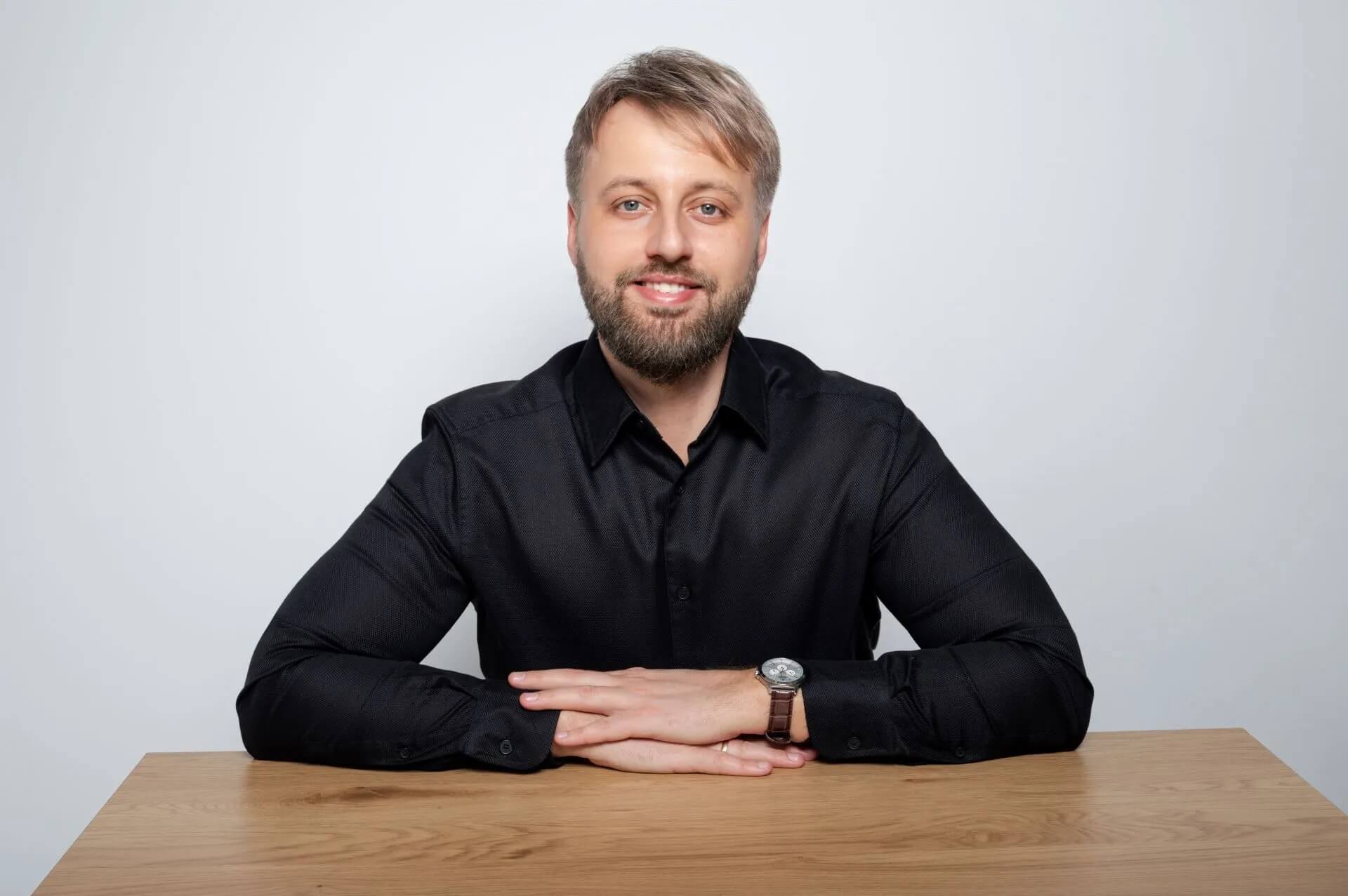 Na zdjęciu widać mężczyznę siedzącego przy biurku, przedstawionego w profesjonalnym ujęciu portretowym. Neutralne tło i formalny strój nadają fotografii biznesowy charakter.